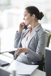 Smiling young businesswoman talking on landline phone in office